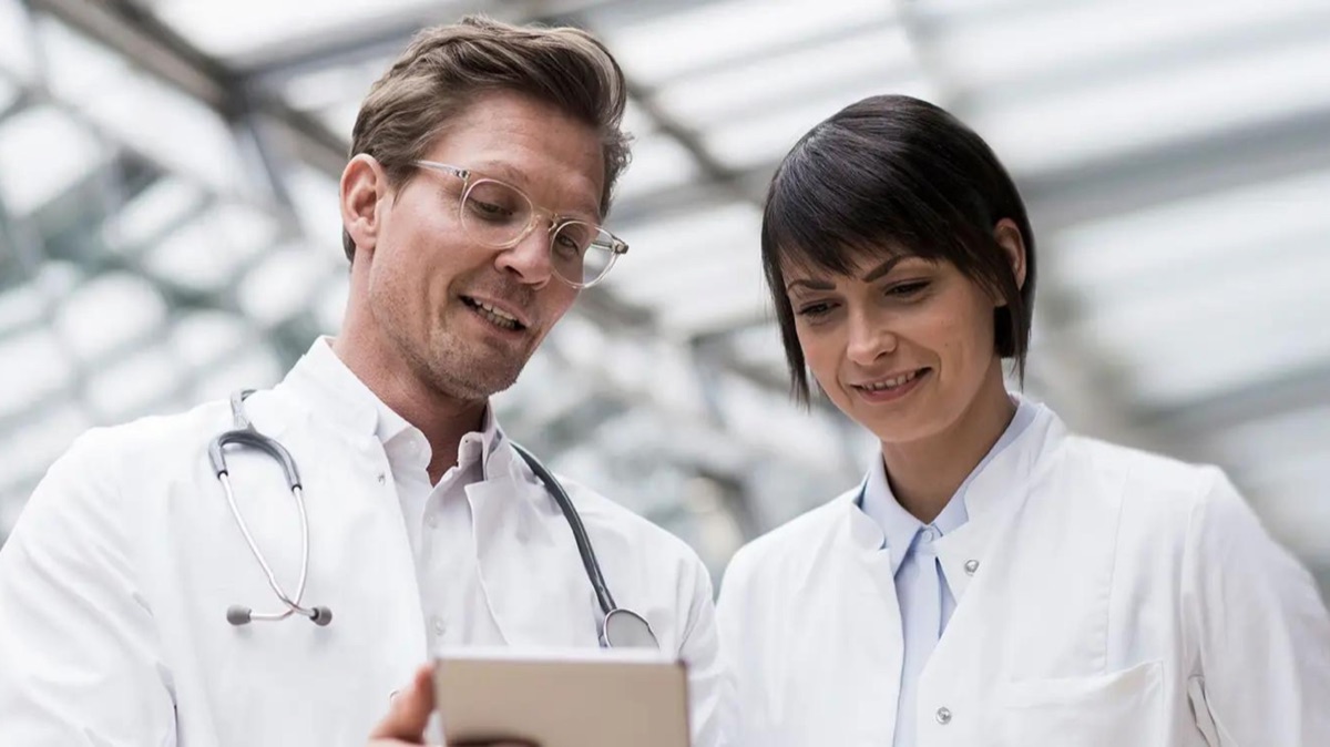 Zwei Ärzt:innen schauen gemeinsam auf ein Tablet, Teamarbeit in der Praxis, Sibel Lang Consulting